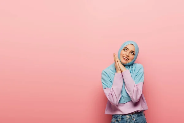 Mujer musulmana feliz en hijab azul mirando hacia otro lado sobre fondo rosa - foto de stock
