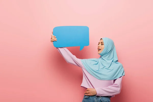 Giovane donna musulmana guardando la bolla discorso blu su sfondo rosa — Foto stock