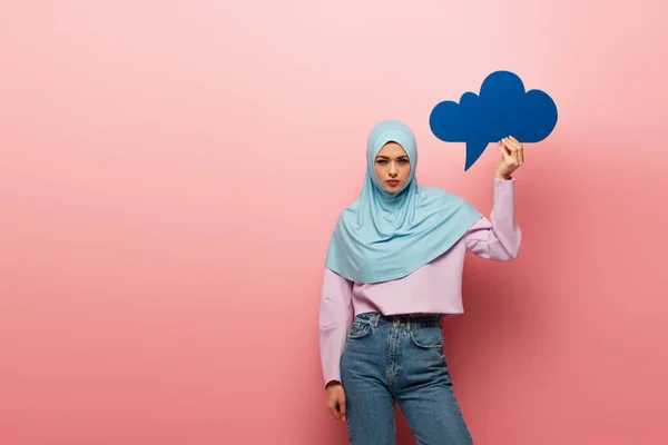 Mujer musulmana en hijab y jeans sosteniendo burbuja pensamiento azul sobre fondo rosa - foto de stock