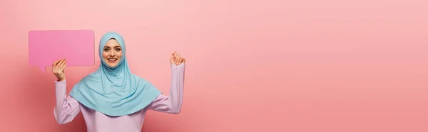Happy muslim woman with blue speech bubble looking at camera on pink background, banner — Stock Photo