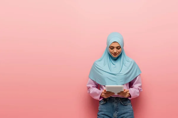 Giovane donna araba in hijab blu utilizzando tablet digitale su sfondo rosa — Foto stock