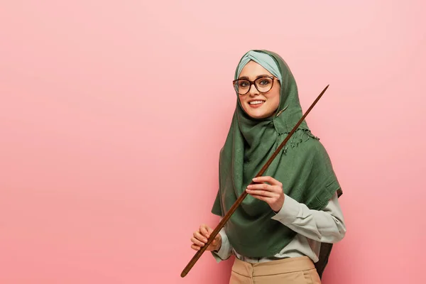 Femme musulmane joyeuse avec bâton de pointage souriant à la caméra isolée sur rose — Photo de stock