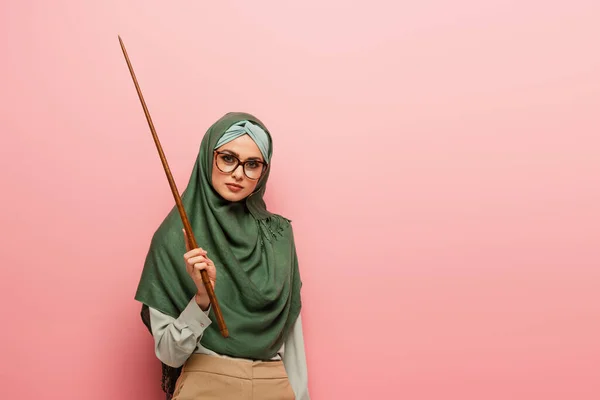 Joven profesor árabe en hijab verde sosteniendo palo puntiagudo aislado en rosa - foto de stock