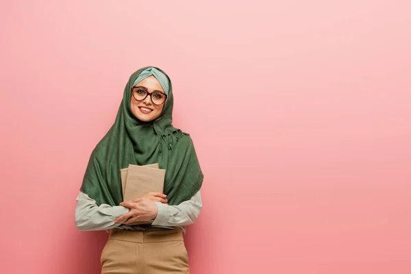 Jolie prof musulmane avec des manuels souriant à la caméra sur fond rose — Photo de stock