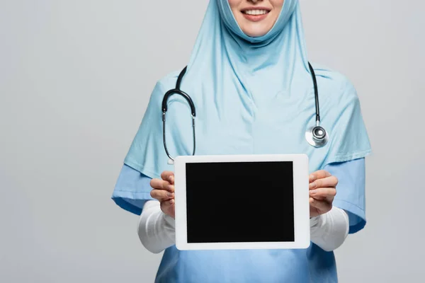 Vista ritagliata di sorridente medico musulmano che mostra tablet digitale con schermo bianco isolato su grigio — Foto stock