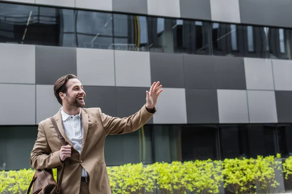 Empresário alegre com saco de couro acenando mão fora — Stock Photo