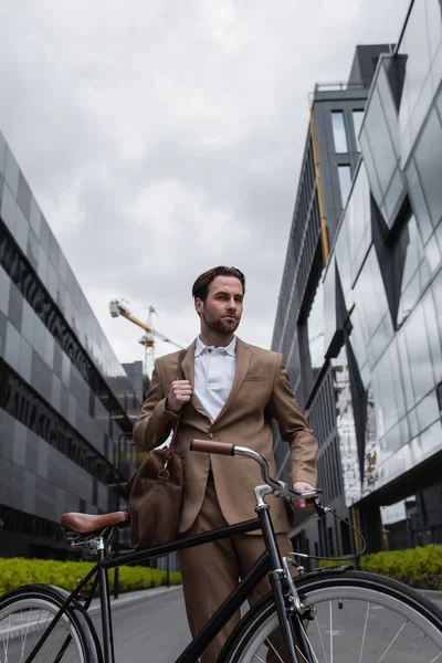 Seriöser Geschäftsmann im Anzug mit Tasche, die neben Fahrrad steht — Stockfoto