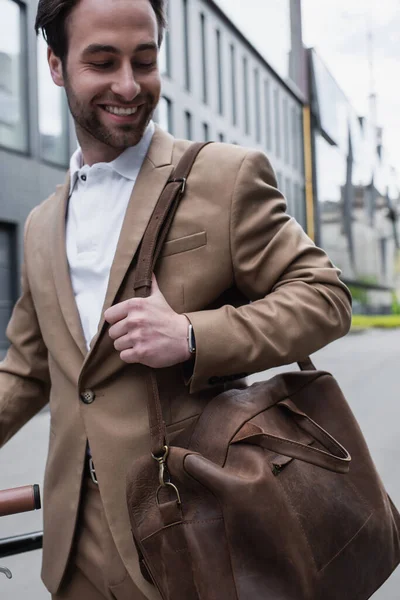 Homem de negócios feliz em terno segurando saco de couro e sorrindo fora — Fotografia de Stock