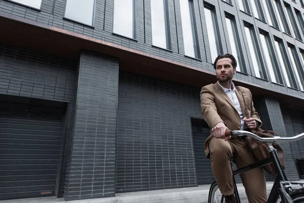 Joven hombre de negocios en traje con bolsa de cuero montar en bicicleta fuera - foto de stock