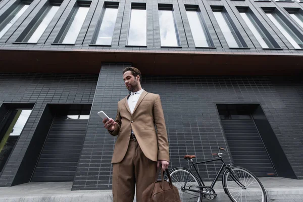 Geschäftsmann im Anzug hält Ledertasche und Smartphone draußen — Stockfoto