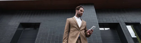 Vue à faible angle de jeune homme d'affaires en tenue formelle à l'aide d'un smartphone à l'extérieur, bannière — Photo de stock