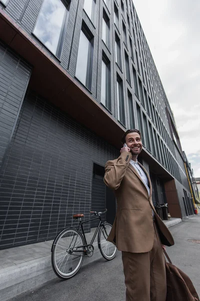 Sonriente hombre de negocios en ropa formal hablando en el teléfono inteligente exterior - foto de stock