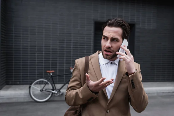 Stressed young businessman in formal wear talking on smartphone outside — Stock Photo