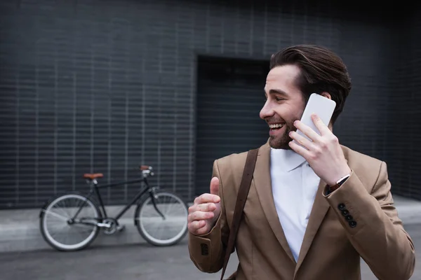 Happy young businessman in formal wear talking on cellphone near building — Stock Photo