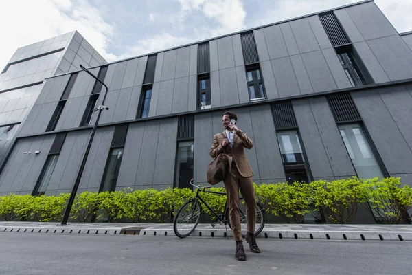 Полная длина счастливый молодой бизнесмен в формальной одежде говорить по сотовому телефону рядом со зданием — стоковое фото