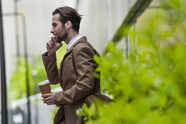 Seitenansicht des Geschäftsmannes in offizieller Kleidung, der auf dem Handy spricht und Pappbecher draußen hält — Stockfoto