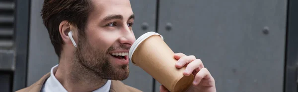 Щасливий бізнесмен в навушниках, що п'ють каву, щоб підійти до будівлі, банер — стокове фото