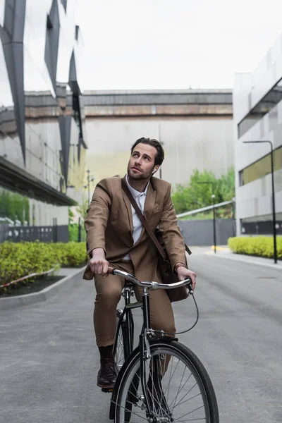 Longitud completa de hombre de negocios en auriculares montar en bicicleta cerca de edificios - foto de stock