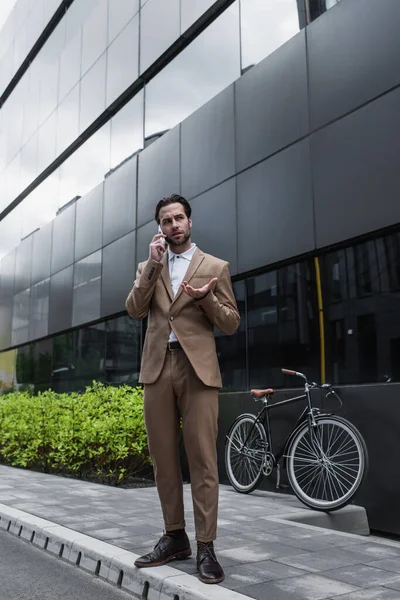 Full length of businessman in suit talking on cellphone near bicycle and building — Stock Photo