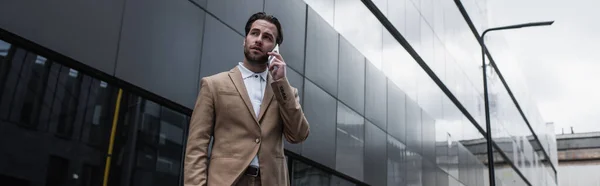 Hombre de negocios hablando en el teléfono celular cerca del edificio, pancarta - foto de stock