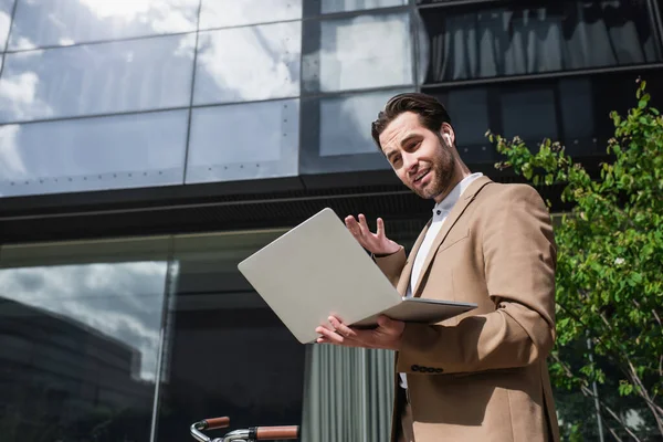 Low angle view of businessman in earphones having video call on laptop outside — Stock Photo