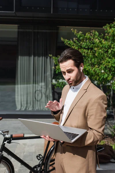 Businessman in earphones having video chat on laptop outside — Stock Photo