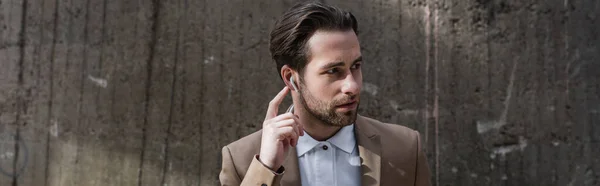 Bearded businessman adjusting earphones near building, banner — Stock Photo