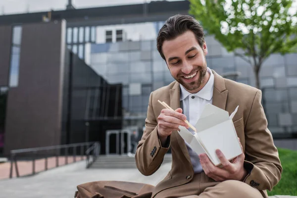 Happy businessman in suit holding cardboard box with thai food and chopsticks — Stock Photo