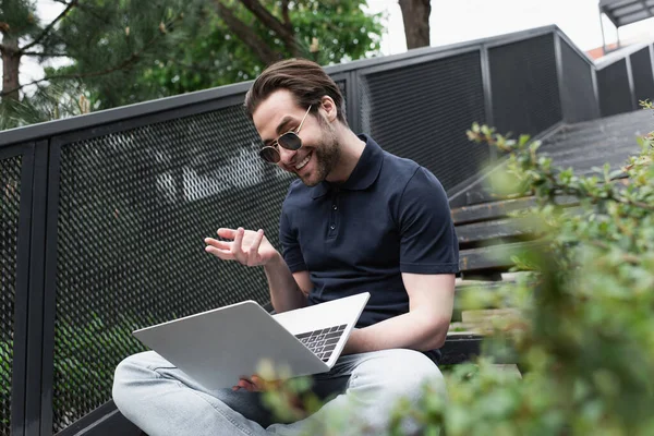 Happy man in sunglasses and polo shirt gesturing while having video chat outside — Stock Photo