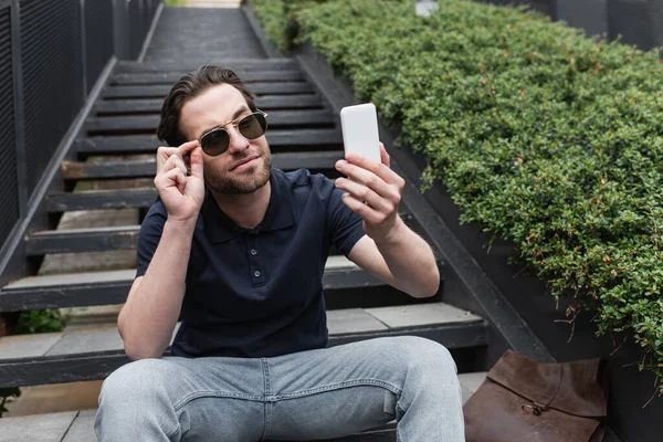 Felice uomo in occhiali da sole e polo prendendo selfie sul cellulare al di fuori — Foto stock