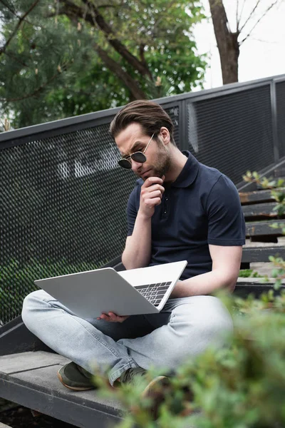 Cher homme regardant ordinateur portable assis avec les jambes croisées sur les escaliers — Photo de stock