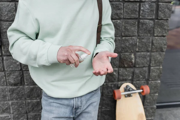 Vista cortada do homem aplicando desinfetante na mão perto de longboard borrado — Fotografia de Stock