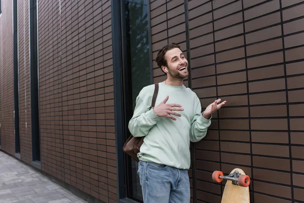 Hombre alegre en sudadera y auriculares inalámbricos hablando y haciendo gestos fuera - foto de stock