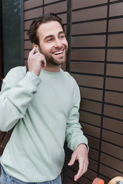 Happy man in sweatshirt adjusting earphone near wall — Stock Photo
