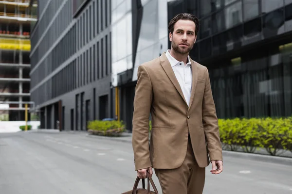 Young businessman in suit holding leather bag on urban street — Stock Photo