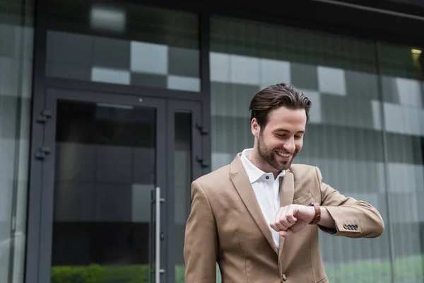 Happy bearded businessman in suit looking at wristwatch — Stock Photo