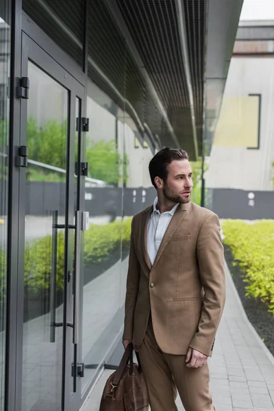 Bärtiger Geschäftsmann in offizieller Kleidung mit Ledertasche in der Nähe eines Gebäudes an der Stadtstraße — Stockfoto