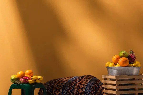 Exotische Früchte auf Hocker und in Metallschale auf orangefarbenem Hintergrund auf orangefarbenem Grund — Stockfoto