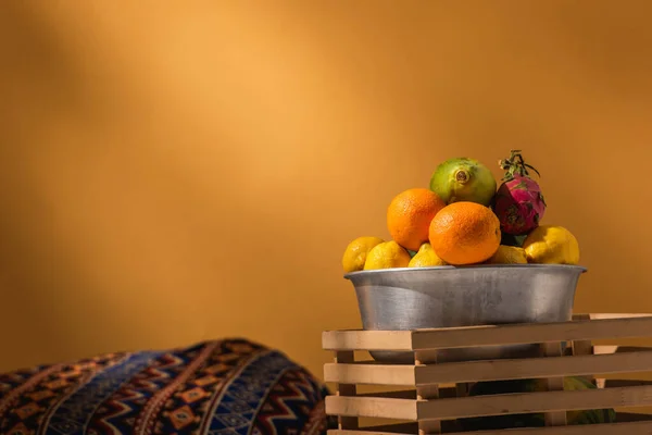 Frutas exóticas em tigela de metal e caixa de madeira perto cobertor ornamento em laranja — Fotografia de Stock