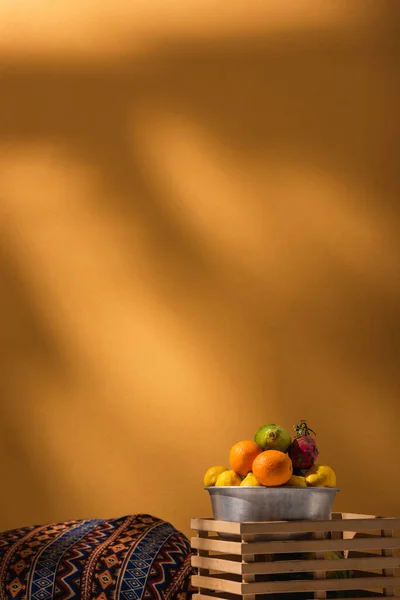 Frutas exóticas em tigela de metal e caixa de madeira perto cobertor com ornamento em laranja — Fotografia de Stock