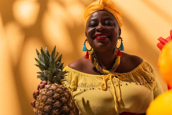 Smiling middle aged african american woman holding pineapple in hand on orange — Stock Photo