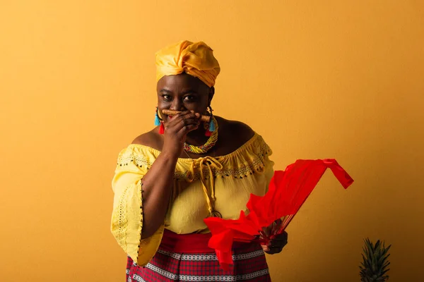 Африканская женщина средних лет в желтом тюрбане и яркой одежде, пахнущей сигарой на желтом — стоковое фото