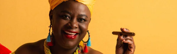 Portrait of smiling middle aged african american woman holding cigar on yellow, banner — Stock Photo