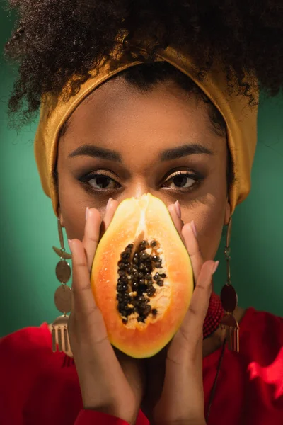 Young african american woman covering face with half cut of ripe papaya on green — Stock Photo