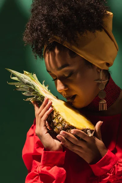 Young african american woman with closed eyes holding half cut of pineapple in hands on green — Stock Photo