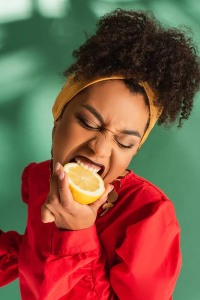 Lächelnde junge afrikanisch-amerikanische Frau isst die Hälfte der Zitrone auf Grün — Stockfoto