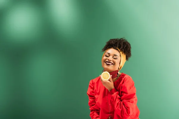 Smiling young african american woman holding half cut of lemon on green — Stock Photo