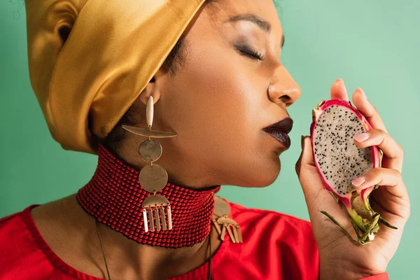 Young african american woman with closed eyes holding half cut of dragon fruit on green — Stock Photo