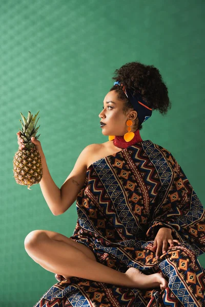 Afrikanisch-amerikanische Frau in Zierdecke eingewickelt hält Ananas auf grünem strukturiertem Hintergrund — Stockfoto