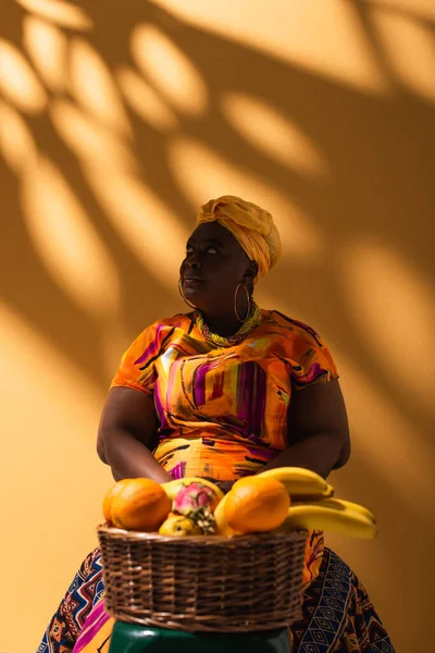 Vendeuse afro-américaine d'âge moyen assise près de fruits sur orange — Photo de stock